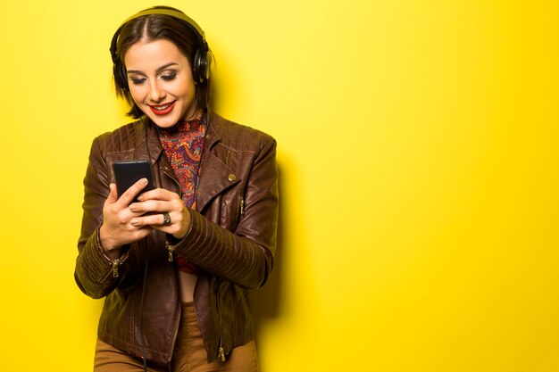 Belle femme appréciant la musique avec les écouteurs dans le mur jaune