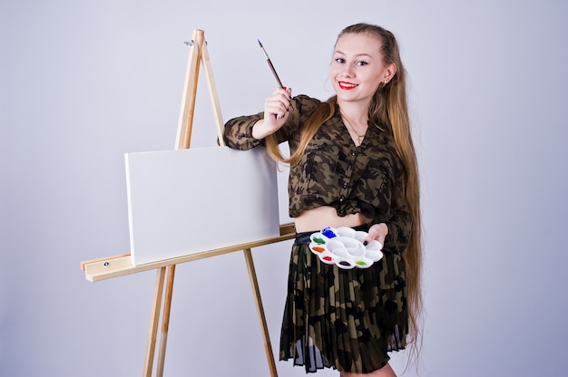 Belle femme artiste peintre avec pinceaux et toile à l'huile posant isolé sur blanc.