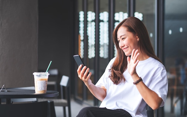 Une belle femme asiatique agitant les mains tout en utilisant un téléphone portable pour un appel vidéo