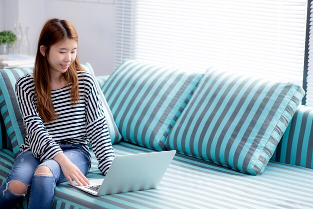 Belle femme asiatique à l&#39;aide d&#39;un ordinateur portable pour les loisirs sur un canapé