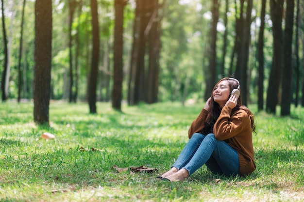 Une belle femme asiatique aime écouter de la musique avec un casque avec un sentiment de bonheur et de détente dans le parc