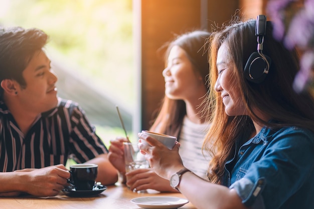 Une belle femme asiatique aime écouter de la musique avec un casque tout en buvant du café avec des amis