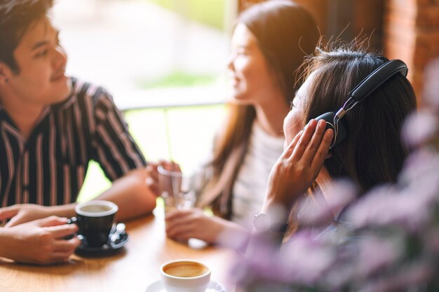 Une belle femme asiatique aime écouter de la musique avec un casque tout en buvant du café avec des amis