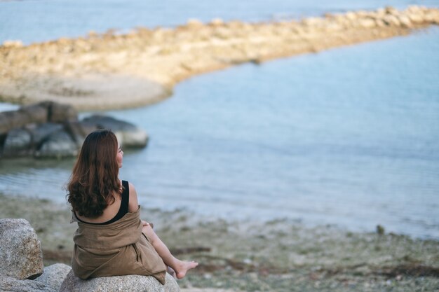 Une belle femme asiatique aime s'asseoir sur le rocher au bord de la mer