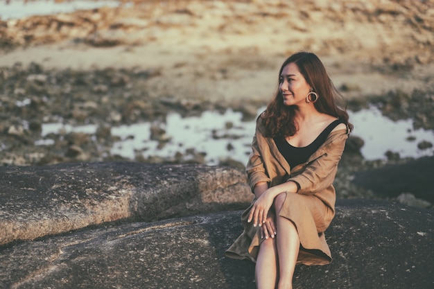 Une belle femme asiatique aime s'asseoir sur le rocher au bord de la mer