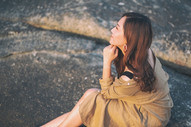 Une belle femme asiatique aime s'asseoir sur le rocher au bord de la mer