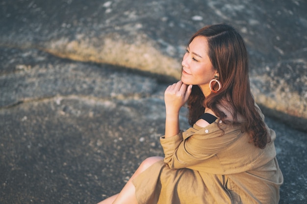 Une belle femme asiatique aime s'asseoir sur le rocher au bord de la mer