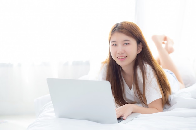 Belle femme asiatique allongée sur le lit à l&#39;aide d&#39;un ordinateur portable dans la chambre