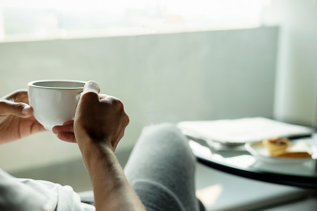 Belle femme asiatique assis dans le lit avec une tasse de café.