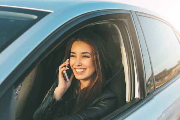 Belle femme asiatique aux cheveux longs brune, conduisant et parlant par téléphone mobile