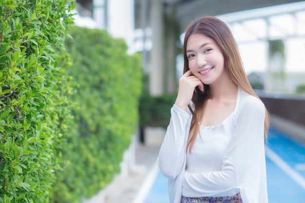 Belle femme asiatique aux cheveux longs en chemise blanche à manches longues se tient à l'extérieur du bâtiment