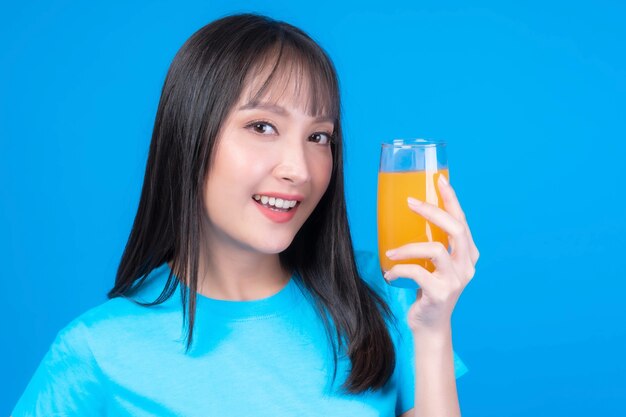 Belle femme asiatique de beauté jolie fille avec une coiffure frange en t-shirt bleu se sentir heureux de boire du jus d'orange pour une bonne santé sur fond bleu - concept sain de femme de beauté de mode de vie