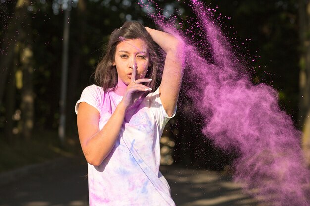 Belle femme asiatique brune tenant le doigt près de ses lèvres jouant avec de la peinture Holi