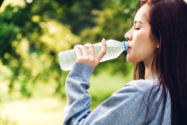 Belle femme asiatique buvant de l'eau provenant d'une bouteille relaxante et fraîche