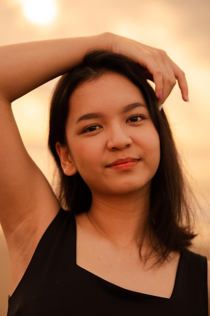 Belle femme asiatique avec une chemise noire et des cheveux noirs souriant avec une peau lisse près de la plage