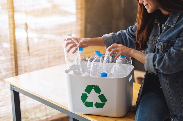 Une belle femme asiatique collecte et sépare les bouteilles en plastique de déchets recyclables dans une poubelle à la maison