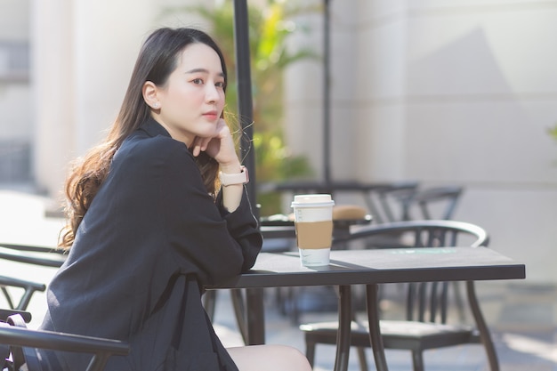 Une belle femme asiatique en costume bleu foncé est assise sur une chaise et sourit joyeusement