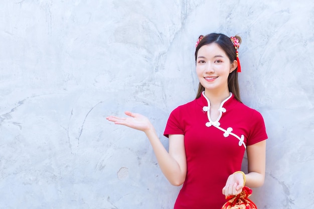 La belle femme asiatique dans la robe rouge se tient pour présenter quelque chose sur le fond gris