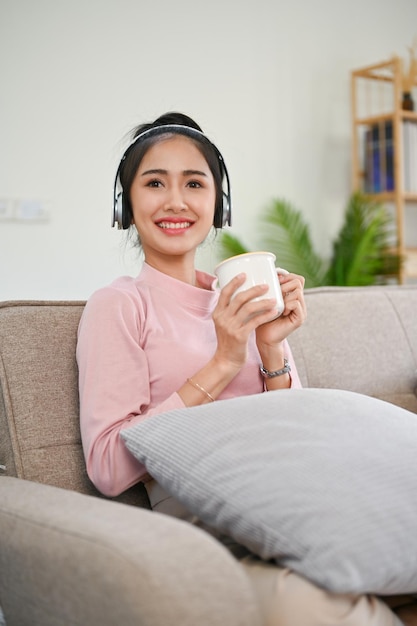 Belle femme asiatique écoutant de la musique tout en sirotant un café le matin sur son canapé