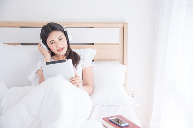 Belle femme asiatique écoute de la musique via le casque tout en étant assis sur le lit