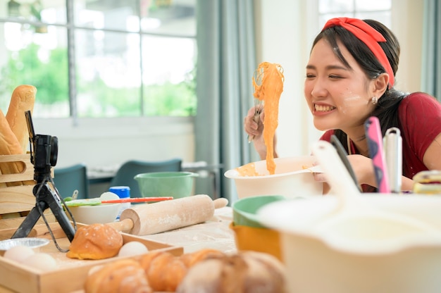 Une belle femme asiatique fait de la boulangerie, diffuse en direct ou enregistre une vidéo sur les réseaux sociaux dans sa maison