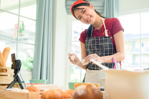 Une belle femme asiatique fait de la boulangerie, diffuse en direct ou enregistre une vidéo sur les réseaux sociaux dans sa maison