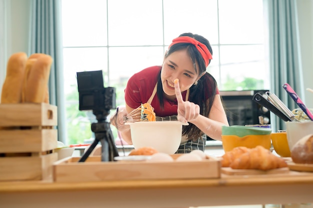 Une belle femme asiatique fait de la boulangerie, diffuse en direct ou enregistre une vidéo sur les réseaux sociaux dans sa maison