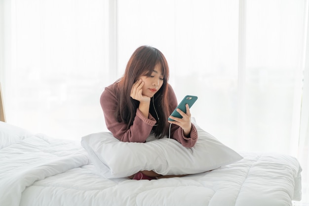 Belle femme asiatique jouant smartphone sur lit