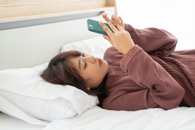 Belle femme asiatique jouant smartphone sur lit