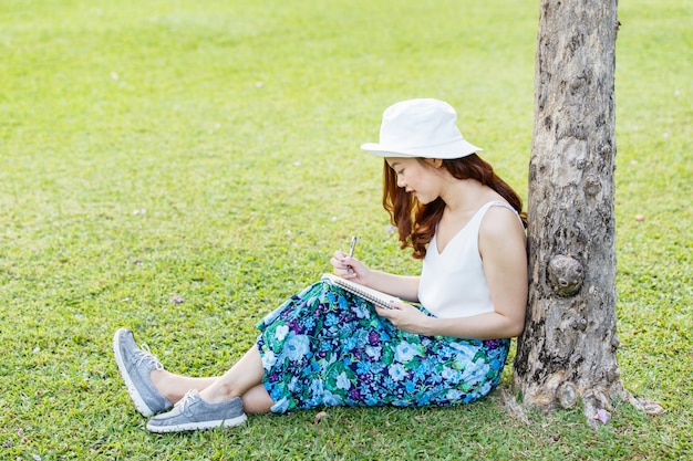 Belle femme asiatique mains avec un stylo écrit un cahier et elle était assise sur l&#39;herbe à l&#39;extérieur