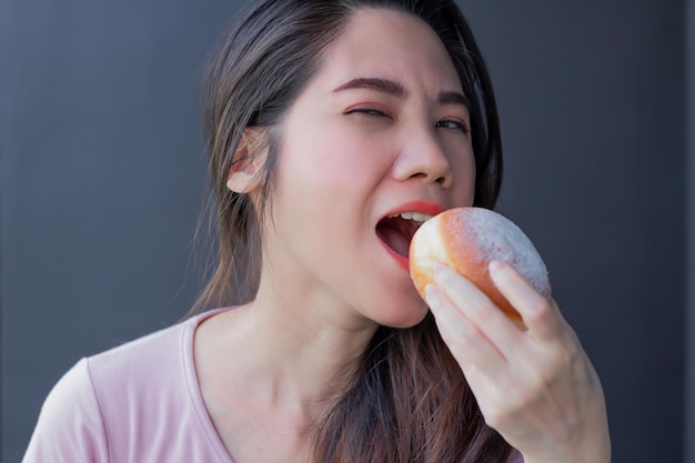 Une belle femme asiatique mange un beignet avec le sourire et le bonheur pendant la pause-café ou le petit-déjeuner