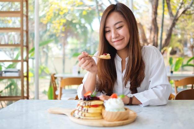 Une belle femme asiatique mangeant de la crème glacée avec des crêpes aux baies mélangées et de la crème fouettée à la cuillère en bois