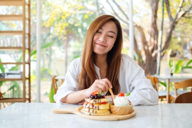 Une belle femme asiatique mangeant de la crème glacée et des crêpes aux baies mélangées avec de la crème fouettée à la cuillère en bois