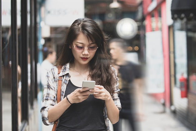 belle femme asiatique marchant sur la rue urbaine et la connexion sur le téléphone intelligent