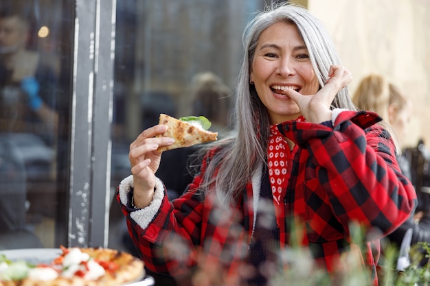 Belle femme asiatique mûrie mange une pizza en terrasse de café