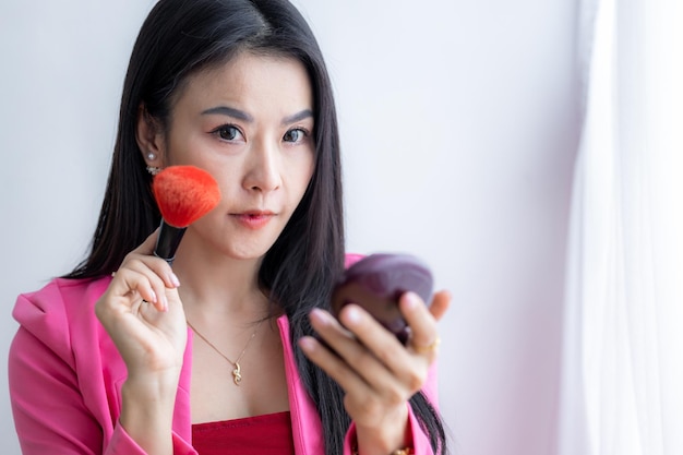 Belle femme asiatique avec des pinceaux de maquillage près du visage et regarder le miroir Beauté asiatique maquillage Jolie fille asiatique tenant des pinceaux de maquillage et maquillage sur le visage avec des cosmétiques à la maison