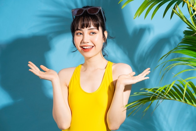 Belle femme asiatique portant une combinaison jaune sur bleu avec des feuilles de palmier