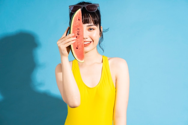 Belle femme asiatique portant une combinaison jaune sur bleu et manger des fruits tropicaux