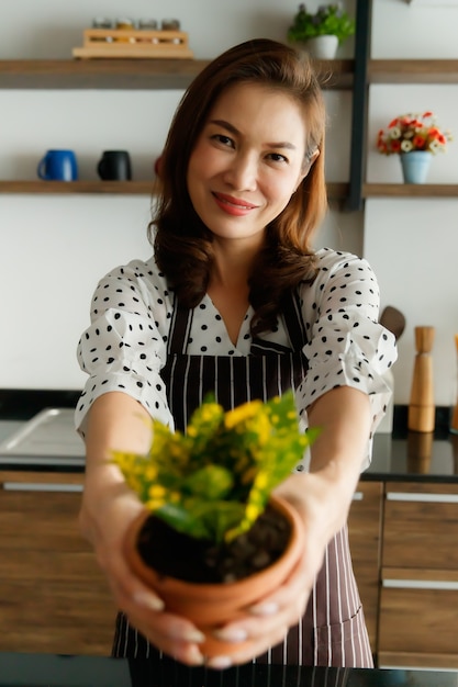 Belle femme asiatique portant un tablier tenant et montrant de petites plantes et fleurs dans le jardin avec un sourire et un visage heureux. Concept de travail de passe-temps et de temps libre.