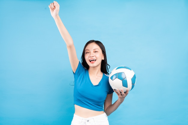 Belle femme asiatique posant avec ballon de foot sur bleu