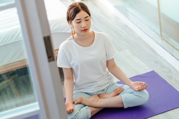 Belle femme asiatique pratiquant la méditation à la maison