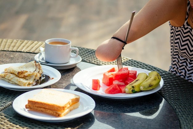 Belle femme asiatique prenant son petit-déjeuner dans un complexe tropical, elle boit une tasse de thé ou de café