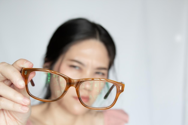 Une belle femme asiatique a un problème de vue et enlève ses lunettes pour vérifier la propreté