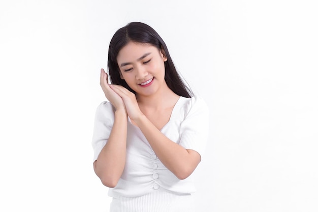 Belle femme asiatique qui a de longs cheveux sourit et montre sa main près du visage sur fond blanc