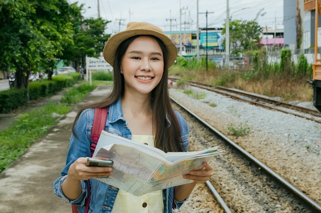 Belle femme asiatique regardant avec enthousiasme la carte de voyage en attendant le train à la gare