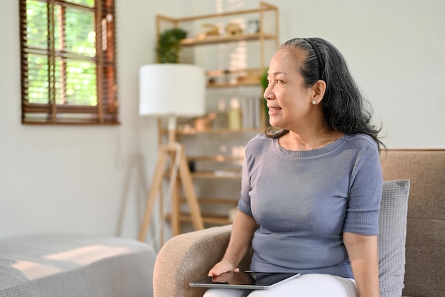 Belle femme asiatique à la retraite regardant par la fenêtre et rêvassant