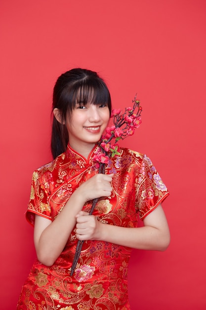 Belle femme asiatique en robe chinoise traditionnelle rouge tenant une branche de sakura