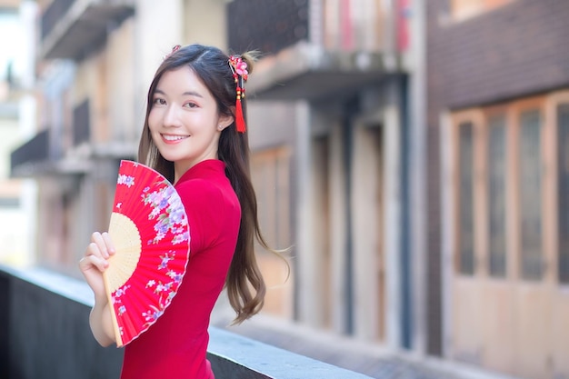 Une belle femme asiatique en robe rouge tient un ventilateur parmi le vieux centre-ville sur le thème du nouvel an chinois