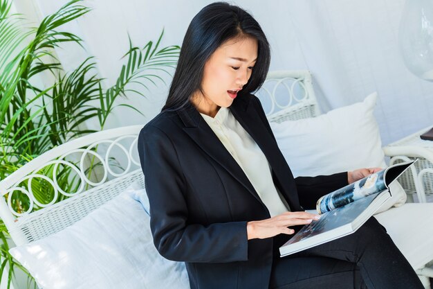 belle femme asiatique s&#39;asseoir se détendre lire livre dans l&#39;intérieur de la chambre blanche et fond de jardin