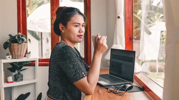 Belle femme asiatique s'assied au comptoir du bar dans un café avec une tasse de café et un sourire